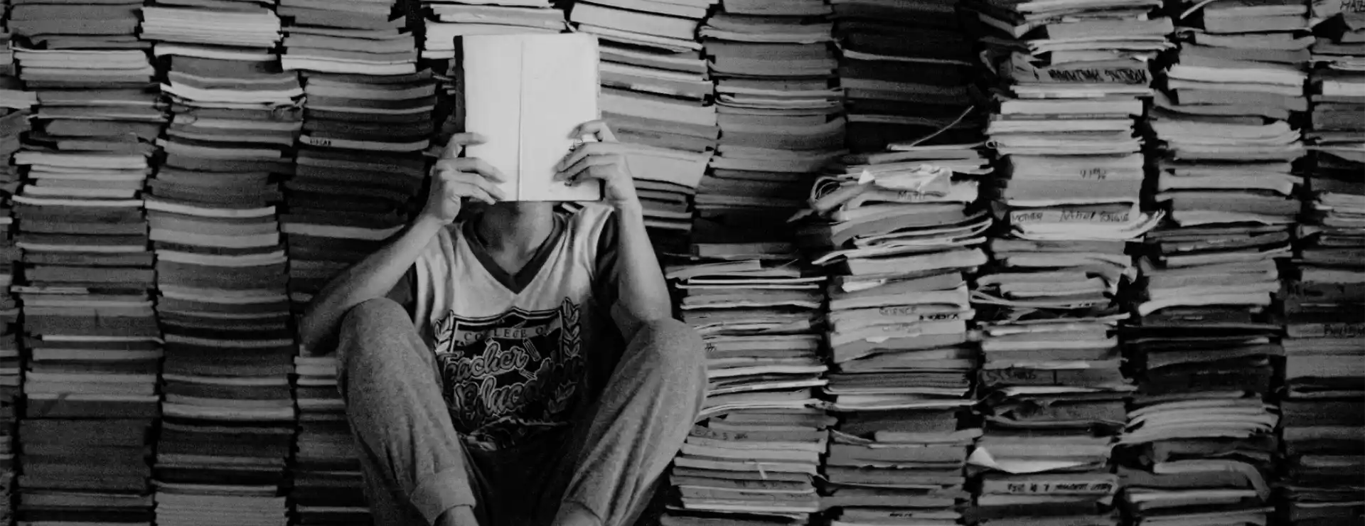 boy sitting reading in front of book pile